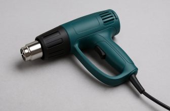 Зелен пистолет за горещ въздух с черна дюза и кабел, поставен върху светлосива повърхност.