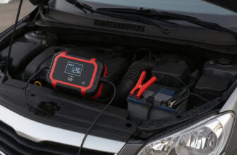 Зарядно устройство е свързано към автомобилен акумулатор под отворения преден капак на кола