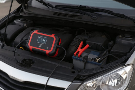 Зарядно устройство е свързано към автомобилен акумулатор под отворения преден капак на кола