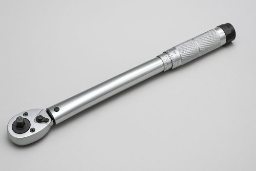 Хромиран динамометричен ключ с релефна дръжка и въртяща се глава, поставен диагонално върху светлосив фон.