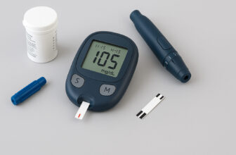 Син глюкомер с ланцет, тест ленти и контейнер, подредени върху светлосив фон