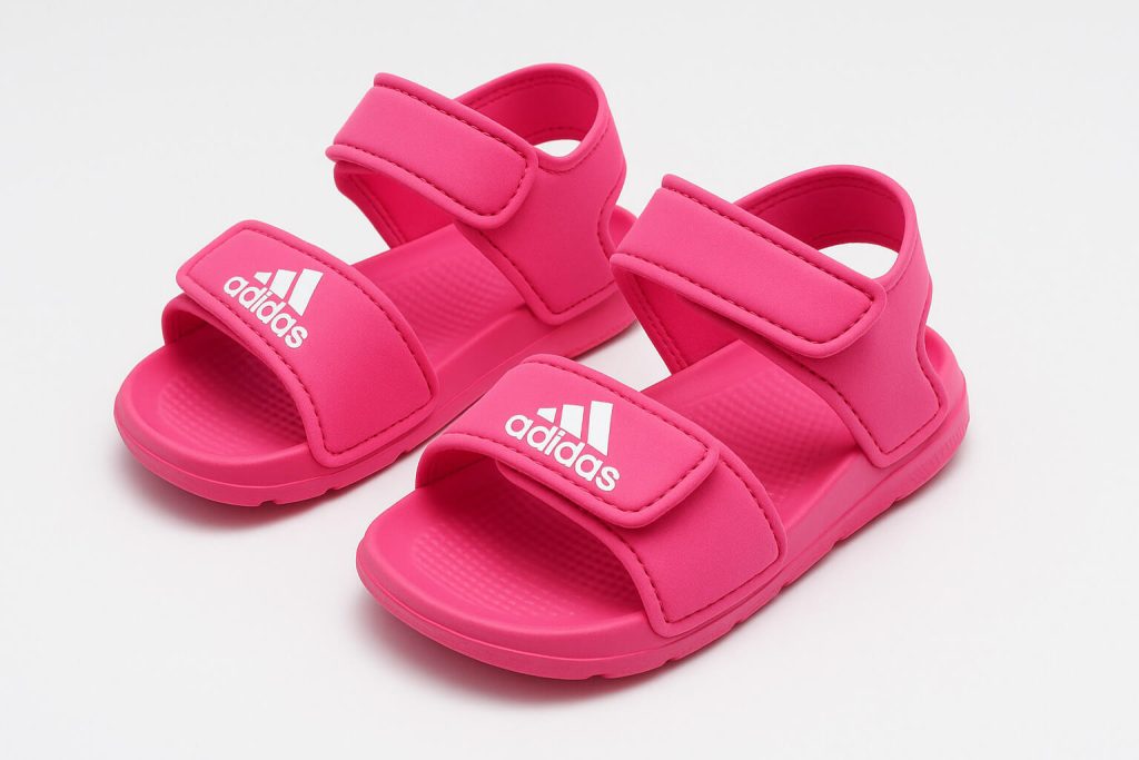 Ярко розови детски сандали Adidas с бяло лого и велкро закопчаване, подредени на бял фон.