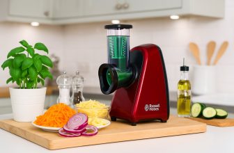 Червено електрическо ренде Russell Hobbs върху дъска с моркови, лук, кашкавал и босилек в модерна кухня.