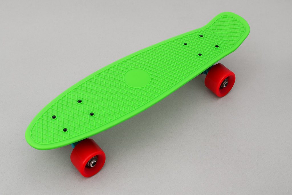 Яркозелен пени борд с червени колела върху сива повърхност