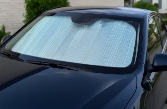 Сребрист сенник отвътре покрива предното стъкло на тъмносиня кола, сниман отвън