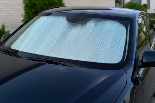 Сребрист сенник отвътре покрива предното стъкло на тъмносиня кола, сниман отвън