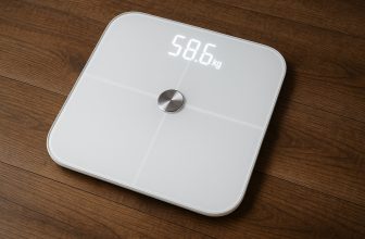 Смарт кантар с бял дисплей, показващ 58.6 kg, върху дървен под